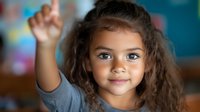 Young mixed race girl with curly brown hair raising hand and smiling confidently in classroom setting, expressing enthusiasm for learning and participation in education.