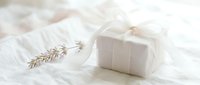 Elegant white gift box tied with a soft ribbon bow beside dried lavender on delicate fabric, perfect for wedding or luxury celebration concepts.