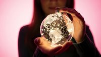 African American woman holding illuminated crystal globe showing world map in cupped hands against pink background for global business concepts.