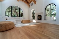 Bright Mediterranean living room with arched black windows, wooden beam ceiling, white fireplace, rattan poufs and hardwood flooring bathed in natural light.