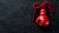 Red boxing glove hanging by lace against dark textured background, dramatic sports equipment composition with copy space for boxing club promotion.
