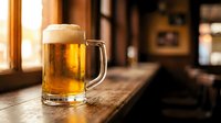 Golden beer mug with foam on wooden bar counter in warm pub atmosphere with sunlight streaming through windows creating cozy drinking establishment ambiance.