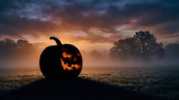 Spooky jack-o-lantern pumpkin glowing in misty field at dramatic sunset for Halloween decorations and seasonal autumn celebrations.
