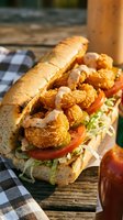 Crispy fried shrimp po boy sandwich with lettuce tomato and remoulade sauce on crusty bread served on rustic wooden table for seafood restaurant menu.