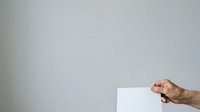 Mature male hand holding blank white card or paper against neutral gray background for mockup and advertising purposes.