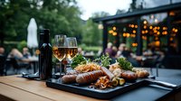 Grilled sausages with sides on black plate, wine glasses and bottle on outdoor restaurant patio table at dusk, ambient string lights and garden atmosphere.