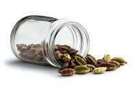 Glass jar spilling fresh green cardamom pods and brown seeds on white background, aromatic spice ingredient for cooking and flavoring food.