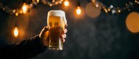 Hand holding a glass of beer with golden bokeh lights in the background, perfect for beverage, celebration, and pub-related designs.