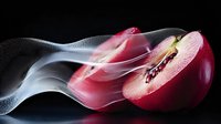 Fresh red apple slice with flowing smoke effect against black background, creating dramatic food photography with contrast and movement.