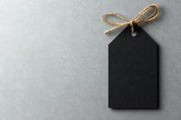 Black blank tag with twine bow on gray concrete background, isolated price label mockup for retail, sale, and gift presentation designs.