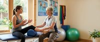 Female physical therapist consulting with senior male patient in modern rehabilitation clinic discussing treatment plan and recovery progress.