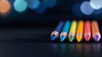 Vibrant colored pencils arranged in rainbow sequence on dark background with soft bokeh lights, creating artistic composition for creative and educational concepts.
