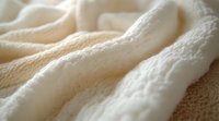 Soft cream-colored fabric with gentle folds and textural details creates cozy, luxurious feeling. Natural light highlights delicate weave pattern and fluffy texture.