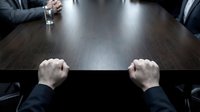 Business meeting tension with clenched fists on conference table during corporate negotiation or difficult discussion in boardroom setting.