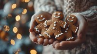 Hands holding freshly baked gingerbread men cookies with smiling faces against blurred Christmas lights background, cozy winter holiday baking mood.