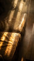 Golden sunlight streaming through window onto vintage leather armchair creating dramatic shadows and warm atmospheric lighting in cozy interior space.