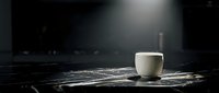 White ceramic cup on black marble surface with dramatic lighting and dark background, suitable for beverage, lifestyle and minimalist design projects.