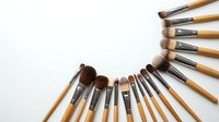 Professional makeup brushes with wooden handles arranged in semicircle on white background for beauty and cosmetics applications.