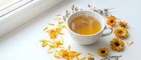 Chamomile tea in white cup with dried flowers and petals on white surface, herbal beverage for relaxation and wellness.