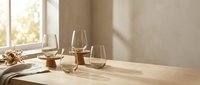 Elegant wine glasses on wooden table with warm sunlight streaming through window creating peaceful dining atmosphere for romantic dinner or celebration.