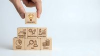 Hand placing wooden block with creativity lightbulb icon on pyramid of business concept blocks including growth, innovation, strategy on white background.