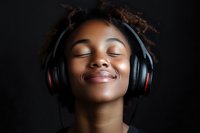 Young African American woman with natural curly hair wearing wireless headphones, eyes closed with peaceful serene expression against dark background.