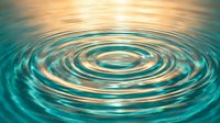 Concentric water ripples creating mesmerizing circular patterns on turquoise surface with golden light reflections for wellness and meditation concepts.
