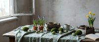Rustic kitchen table with fresh green apples, potted plants, ceramic bowls and vintage linens creating cozy farmhouse atmosphere for food styling.