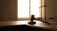 Wooden gavel and brass scales of justice on desk in warm sunlit courtroom setting for legal and law firm presentations.