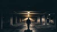 Silhouette of man standing in dark underground parking garage with dramatic lighting creating atmospheric mood for mystery and suspense themes.