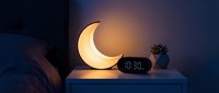 Glowing crescent moon lamp on bedside table with digital clock creating warm ambient lighting for cozy bedroom nighttime atmosphere and relaxation.