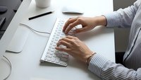 Professional businesswoman typing on white wireless keyboard at modern office desk workspace for productivity and remote work applications.