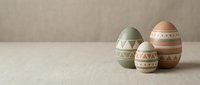 Three decorative Easter eggs with geometric patterns in soft pastel colors arranged on neutral textured surface for spring holiday celebrations.