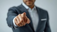 Middle Eastern businessman in dark suit pointing finger directly at viewer, professional corporate portrait with selective focus on hand gesture. Leadership concept.