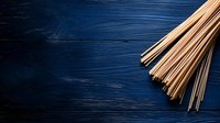 Raw brown rice noodles on dark blue wooden background with copy space, overhead view of traditional Asian ingredients for cooking oriental cuisine.