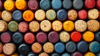 Colorful wine bottle corks arranged in rows creating abstract pattern background. Variety of natural and synthetic corks in red, blue, orange and yellow colors.