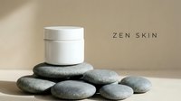 White cosmetic jar with lid positioned on stacked smooth gray stones against neutral beige background, representing zen skincare and natural beauty products for spa and wellness branding.