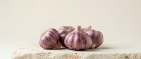 Red onions with papery skin arranged on a rustic stone surface against neutral background, suitable for food photography, culinary content, and healthy eating concepts.