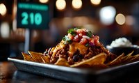 Loaded nachos topped with melted cheese, seasoned meat, fresh pico de gallo and garnished with herbs on metal plate against dark restaurant background with bokeh lights.