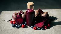 Fresh beetroot juice in glass bottle with raw beets, berries and vegetables on concrete surface for healthy organic nutrition and detox lifestyle.