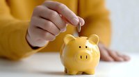 Woman in yellow sweater putting coin into golden piggy bank for savings and financial planning goals.