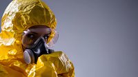 Person wearing yellow hazmat protective suit and respirator mask against gray background, safety equipment for chemical, biological or nuclear protection.