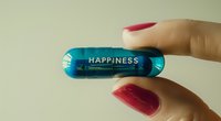 Female hand with red manicure holding blue transparent pill capsule with happiness text, mental health and antidepressant medication concept.