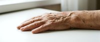 Elderly male hand with age spots and wrinkles resting on white surface, depicting aging, senior care, and healthcare topics for medical and wellness content.