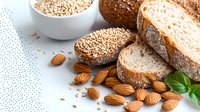 Fresh sliced whole grain bread with scattered almonds, sesame seeds and basil leaves on light background, healthy breakfast concept.