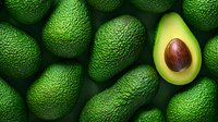 Fresh ripe green avocados background with one cut avocado half showing brown pit and creamy flesh, top view arrangement for healthy food concept.