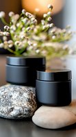 Black cosmetic jars with natural stones and delicate white flowers create zen spa composition against blurred background. Luxury skincare packaging concept.
