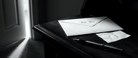 Black and white moody scene of a handwritten envelope labeled For You on a wooden desk with a pen, evoking mystery, romance, or farewell.