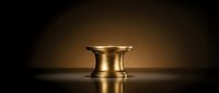 Golden brass mortar bowl with elegant curved design on dark surface with dramatic lighting for kitchen cooking and food preparation.