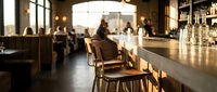 Wooden bar stools lined up at counter in modern restaurant or lounge with blurred staff and patrons in background, suitable for hospitality and interior design projects.